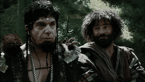 two men are standing next to each other in a forest