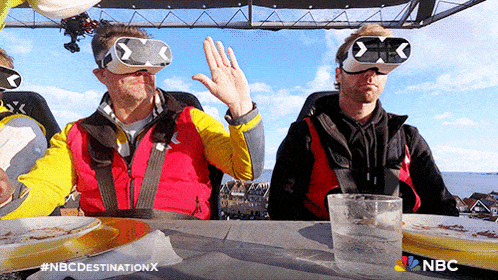 two men wearing virtual reality glasses are sitting at a table eating