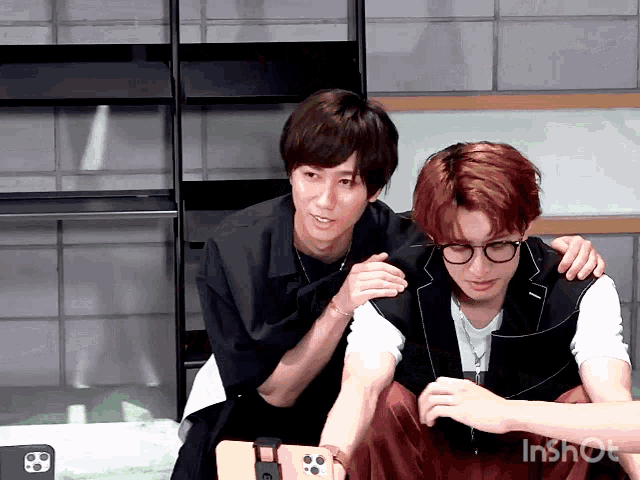 two young men are sitting next to each other and one of them is looking at a cell phone