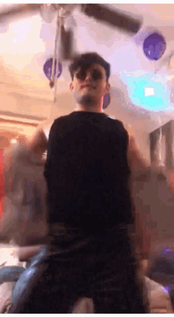 a man wearing sunglasses and a black shirt is standing in a room with a ceiling fan