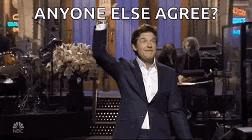 a man in a suit is standing on a stage with his arm in the air and asking anyone else to agree .