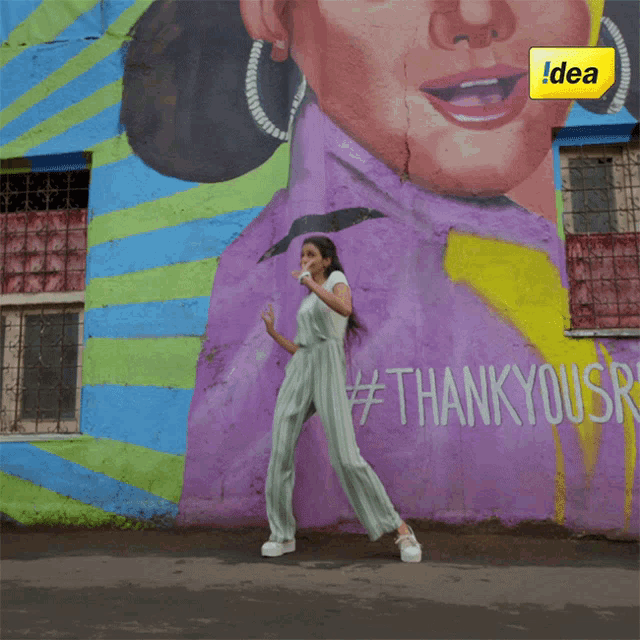 a woman stands in front of a mural that says thank you