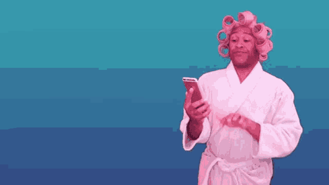 a man in a bathrobe and curlers is looking at his phone .