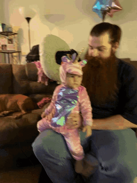 a man with a beard holds a baby in a unicorn costume