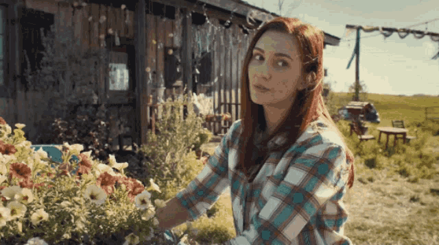 a woman in a plaid shirt is standing in a garden