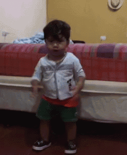 a little boy is standing in front of a bed wearing a white shirt and green shorts