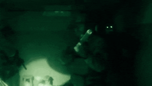 a soldier is standing in a dark room holding a rifle and a flashlight .