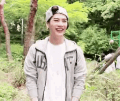 a young man wearing a beanie and a jacket is standing in the woods .