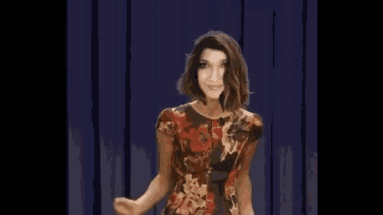 a woman in a floral dress is standing in front of a blue curtain .