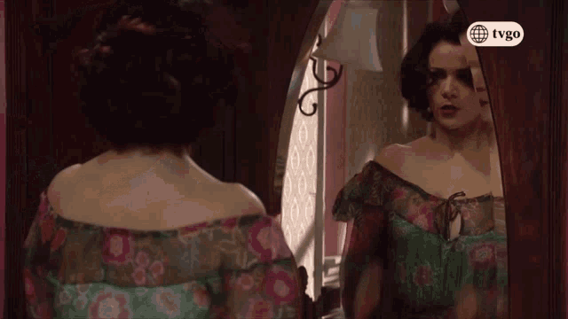 a woman looking at herself in a mirror with a tvgo logo on the bottom