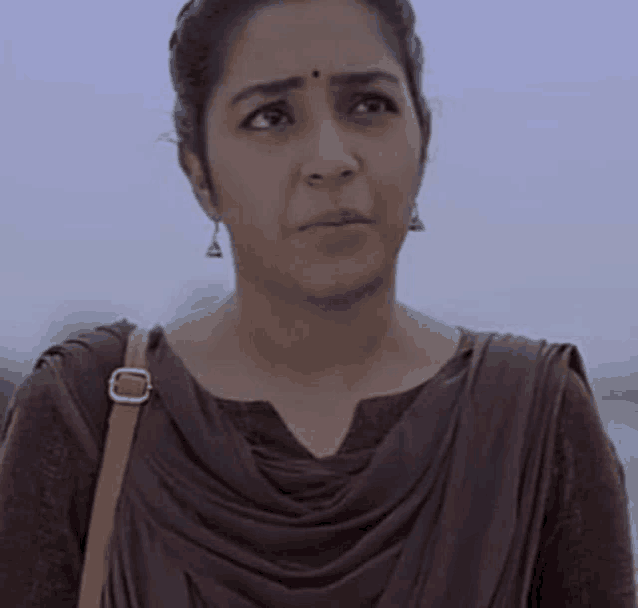 a woman wearing a brown dress and earrings is looking at the camera .