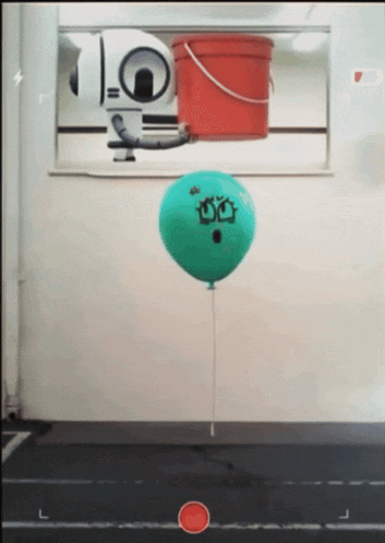 a green balloon with a face drawn on it is floating in the air