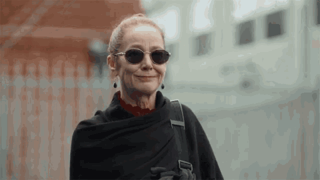 a woman wearing sunglasses and a black scarf smiles at the camera
