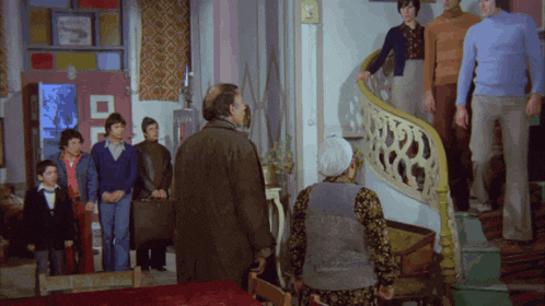 a group of people are standing in a room with a staircase leading up to the second floor