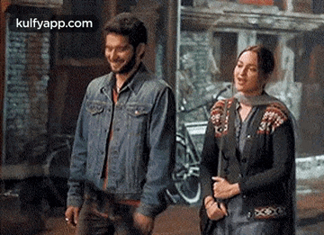 a man and a woman are standing next to each other on a street holding hands and smiling .
