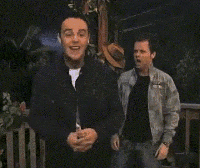 a man in a gray jacket and black shirt is standing on a porch .