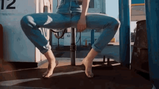 a person is squatting down with their legs crossed in front of a gas pump with the number 12 on it