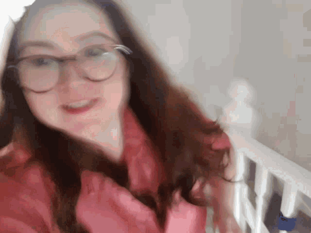 a woman wearing glasses and a pink sweater is smiling