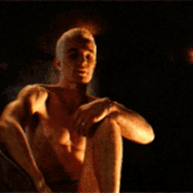 a shirtless man sits on a chair with his legs crossed