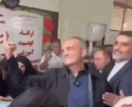 a group of people are standing in a room with their hands in the air and one man is giving the middle finger .