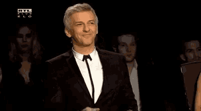 a man in a suit and tie is smiling while standing in front of a crowd .