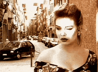 a woman is standing on a street with cars parked on the side