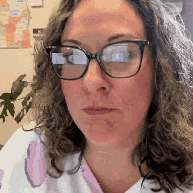 a woman wearing glasses looks at the camera with a map on the wall in the background