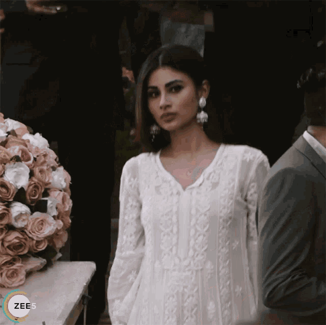 a woman in a white dress is standing in front of a bouquet of flowers and a sign that says zee5