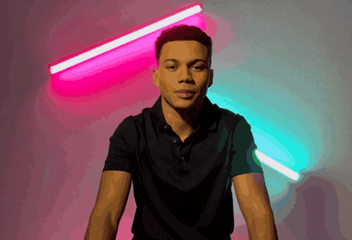 a young man in a black shirt is standing in front of a pink and blue light