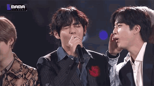 a man holding a microphone next to another man with the word mama on the bottom right