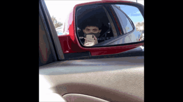 a man wearing a mask is taking a picture of himself in the rear view mirror of a car