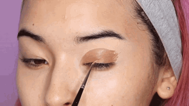 a woman with pink hair is applying eye shadow