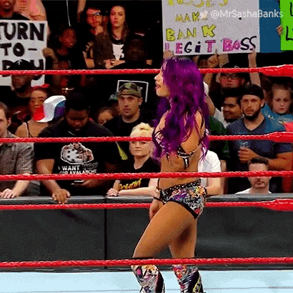 a woman with purple hair is standing in a wrestling ring with a crowd behind her .
