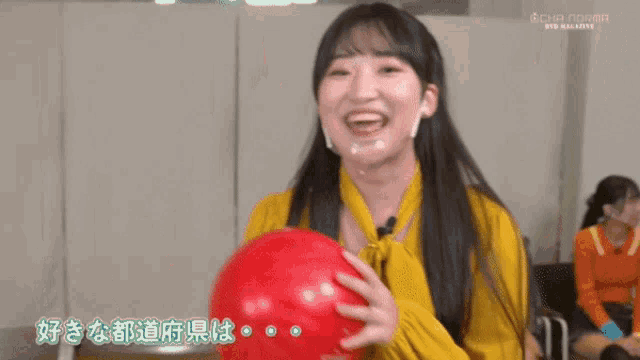 a girl in a yellow shirt is holding a red bowling ball and smiling