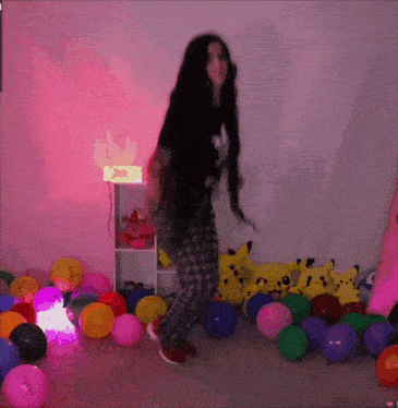 a woman is dancing in front of a pile of balloons one of which has the word balloon on it