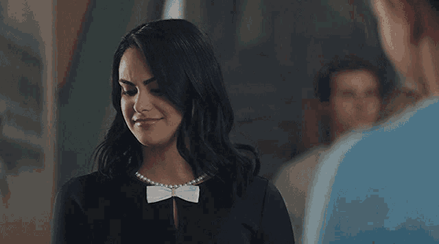 a woman wearing a pearl necklace and a bow tie is looking at a man in a blue shirt .