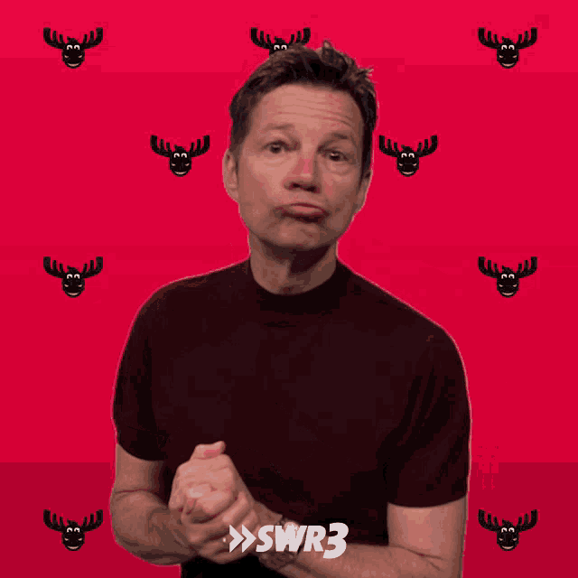 a man with a watch on his wrist is smiling in front of a red background with moose faces on it
