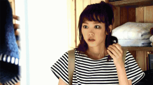 a woman in a striped shirt is standing in front of a mirror looking at her hair .