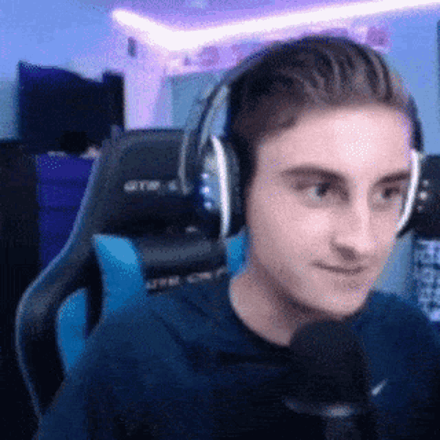 a man wearing headphones and a blue shirt is sitting in a chair talking into a microphone .