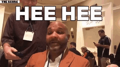 a bald man in a suit says hee hee in front of a group of people