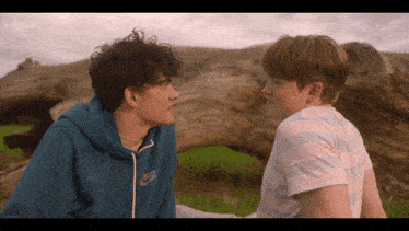 a boy wearing a blue nike sweatshirt sits next to a boy wearing a pink and white striped shirt