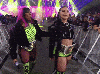 two women are standing next to each other in front of a crowd and one has pink hair .