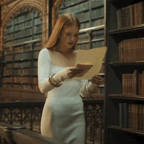 a woman in a white dress is holding a piece of paper in a library .