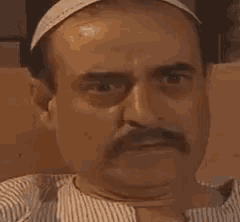 a close up of a man with a mustache wearing a hat and a striped shirt .