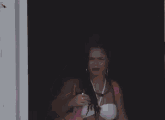 a woman in a bikini is standing in front of a black wall holding a pink bag .