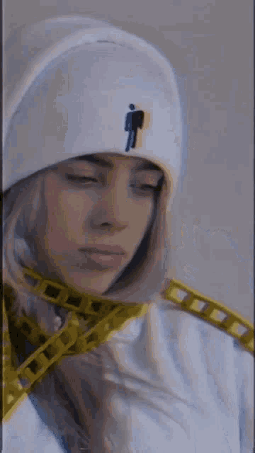 billie eilish is wearing a white hat and a white hoodie .