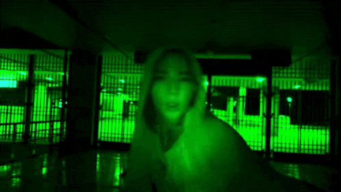 a woman covering her mouth with her hand in a dark room with green lights behind her