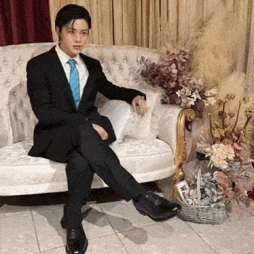 a man in a suit is sitting on a couch with his legs crossed .