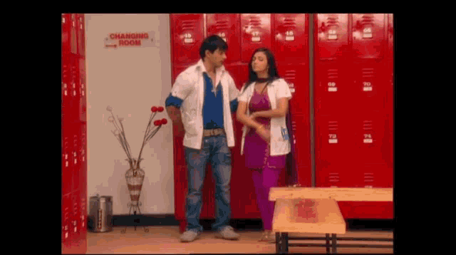 a man and a woman are standing in a changing room with red lockers