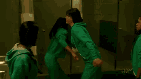 a group of people in green jumpsuits are standing in a bathroom looking at each other .
